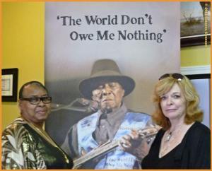 Suzanne Swanson and Honeyboy's eldest daughter, T-Baby stand with a large banner of the blues music master